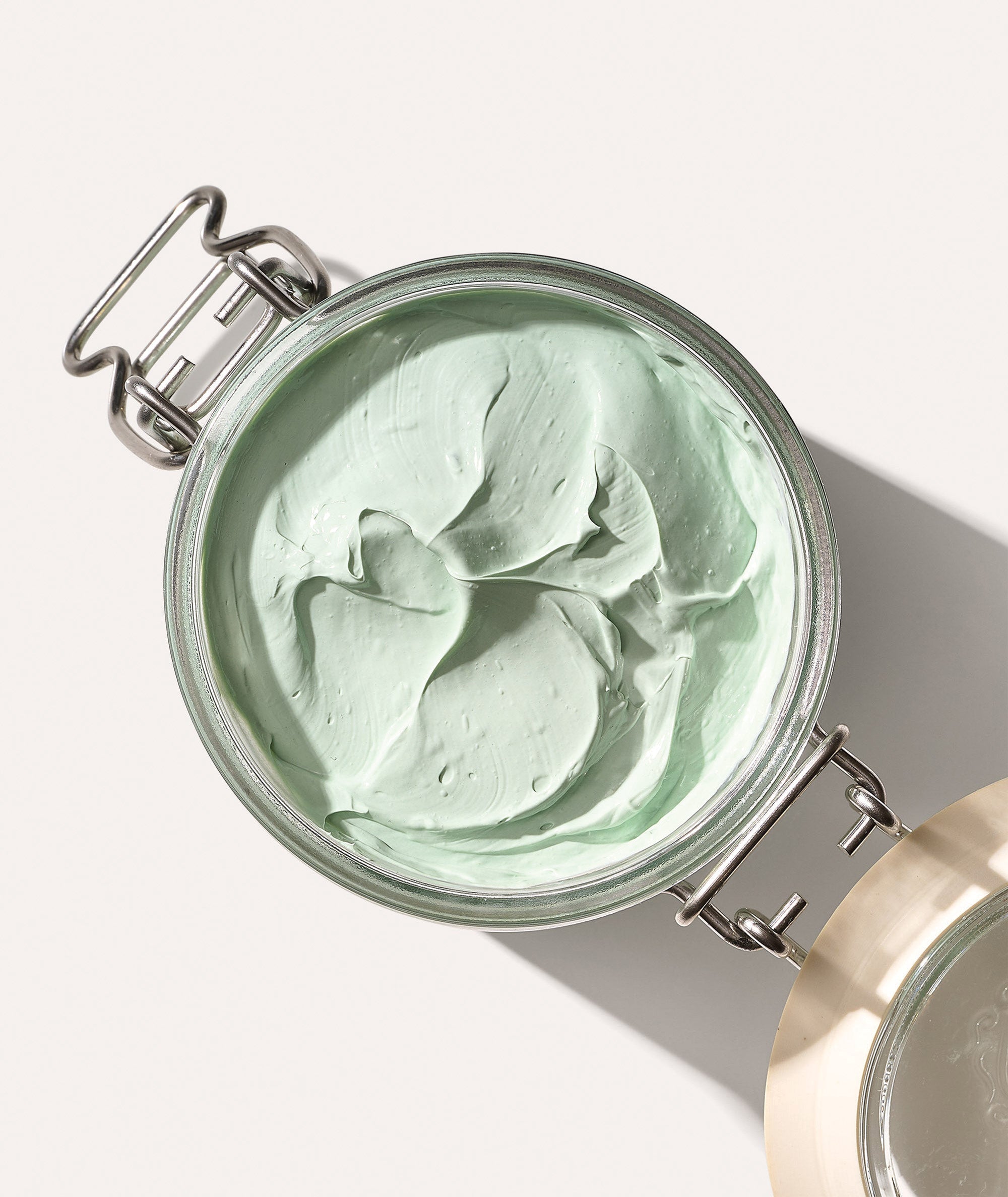 Open Fango Delicato glass jar showing the mint green color and thick texture of the mud mask